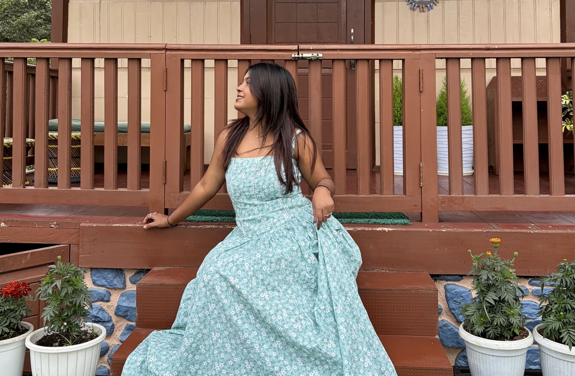 A model in a mint green floral dress sitting on garden steps in front of a wooden railing